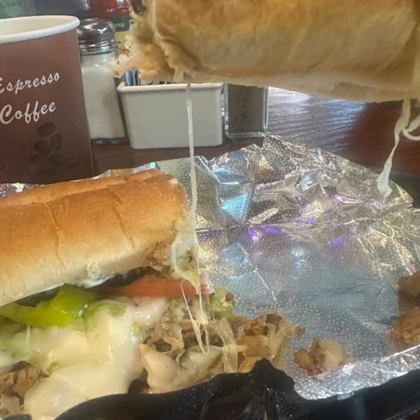 A cheesy steak and cake sandwich with melted cheese stretching, next to an "Espresso Coffee" cup.