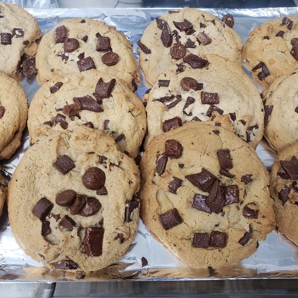 Freshly baked chocolate chip cookies with large chunks of chocolate on a foil-lined tray.
