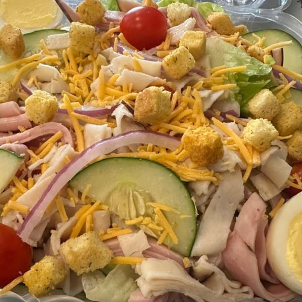 Close-up of a chef salad with lettuce, ham, turkey, cheese, cucumbers, tomatoes, croutons, and egg.