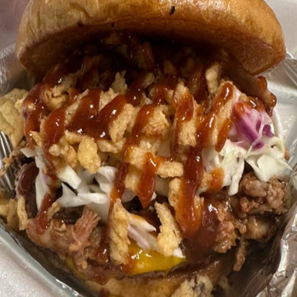 Close-up of a pulled pork sandwich with coleslaw, crispy onions, and BBQ sauce on a bun.