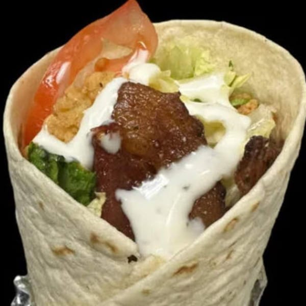 A close-up of a wrap filled with steak, lettuce, tomato, and white sauce, from STL Steak and Cake.