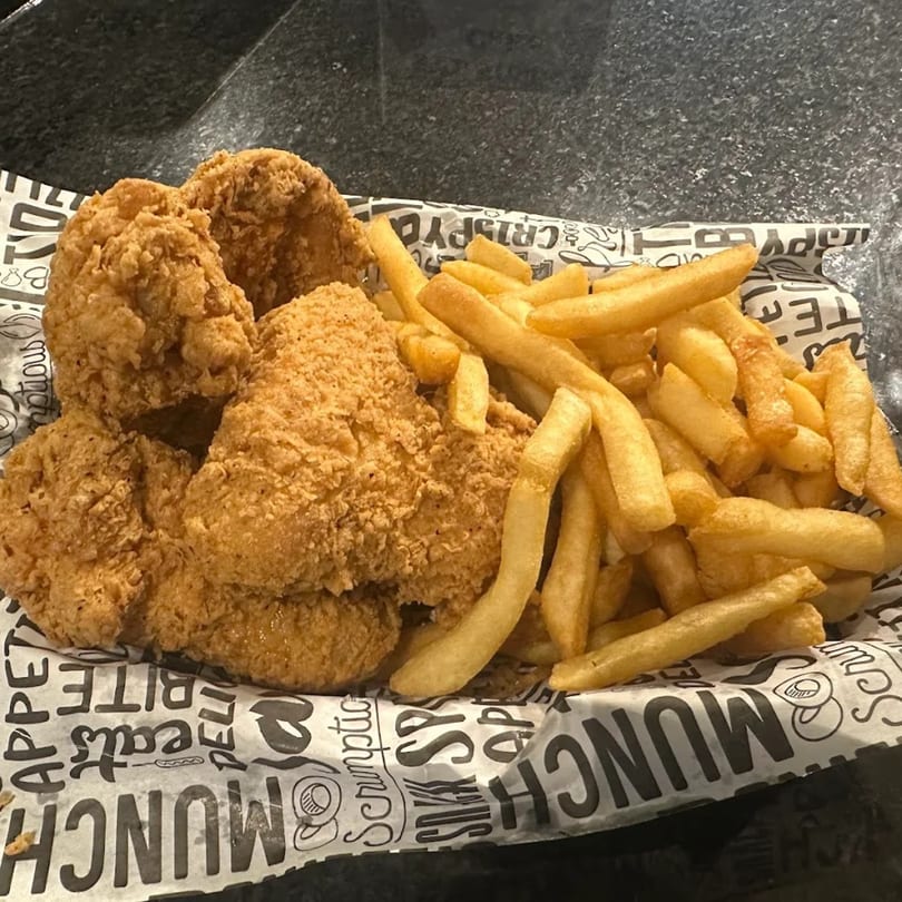 Crispy fried chicken pieces and golden french fries served on branded paper in a basket.