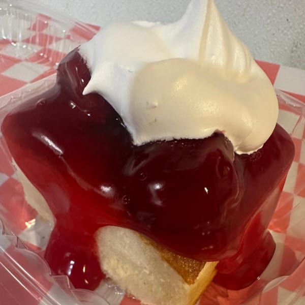 A slice of cake topped with bright red cherry pie filling and a dollop of white whipped cream.