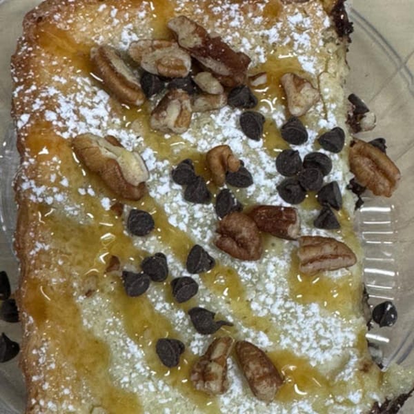 Close-up of a dessert bar topped with powdered sugar, honey, pecans, and chocolate chips.