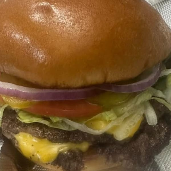 Close-up of a STL Steak and Cake cheeseburger with lettuce, tomato, onion, and pickles.