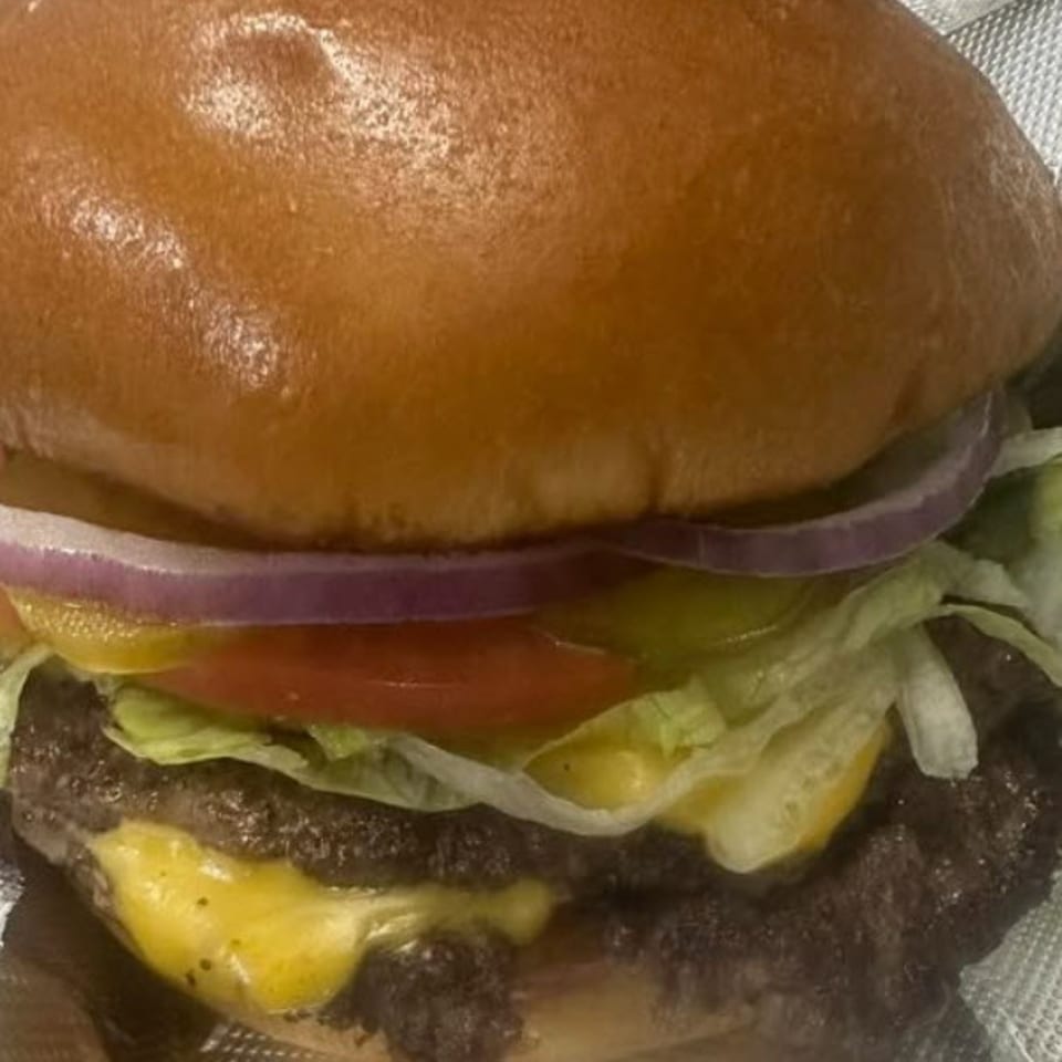 Close-up of a STL Steak and Cake cheeseburger with lettuce, tomato, onion, and pickles.